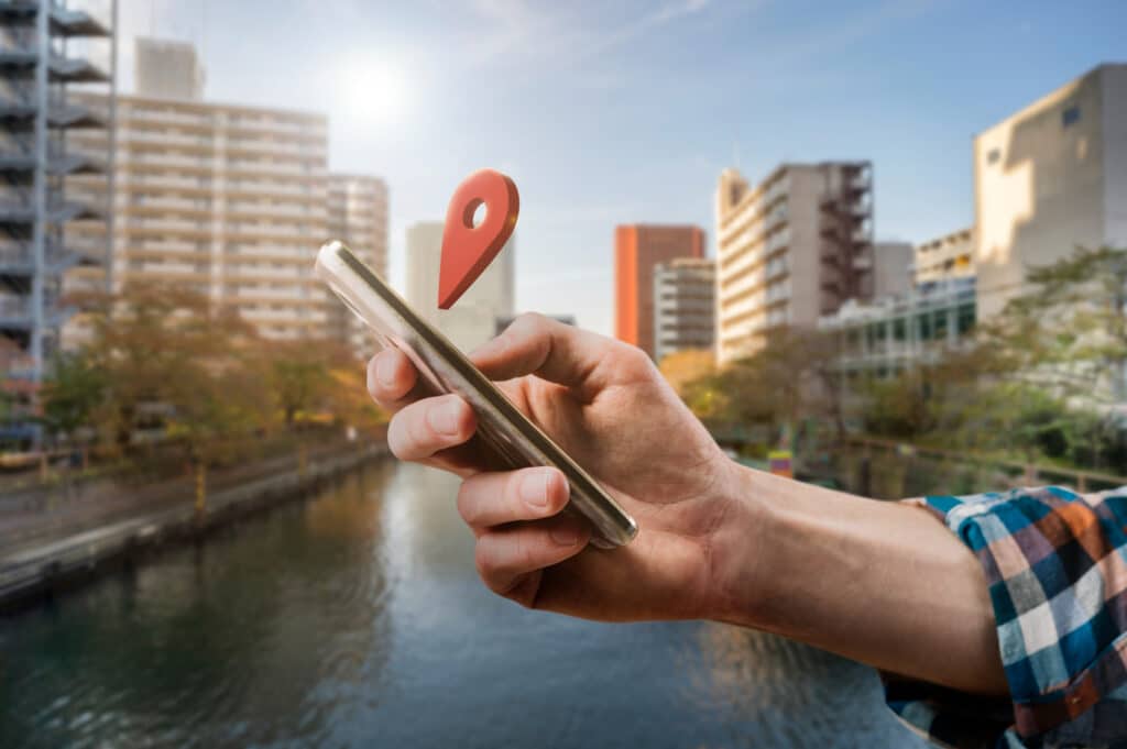 Persona che tiene in mano uno smartphone con un'icona di localizzazione sovrapposta, con sfondo urbano